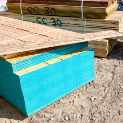 Stosy drewnianych desek i sklejka na wymiar leżą na placu budowy.