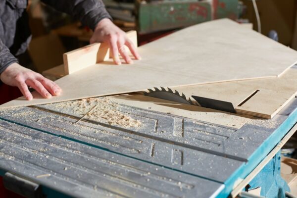 Stolarz przycina sklejkę na wymiar na pile tarczowej.